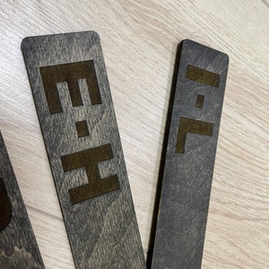Puede incluir: Tres letreros rectangulares de madera con pintura negra y letras marrones. Los letreros dicen "E", "H" e "I".