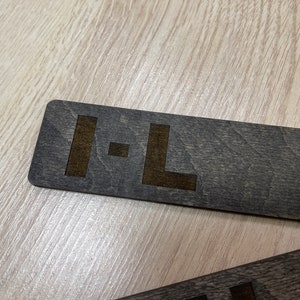 Puede incluir: Un letrero de madera gris oscuro con las letras "I-L" grabadas en un color marr&oacute;n m&aacute;s claro.