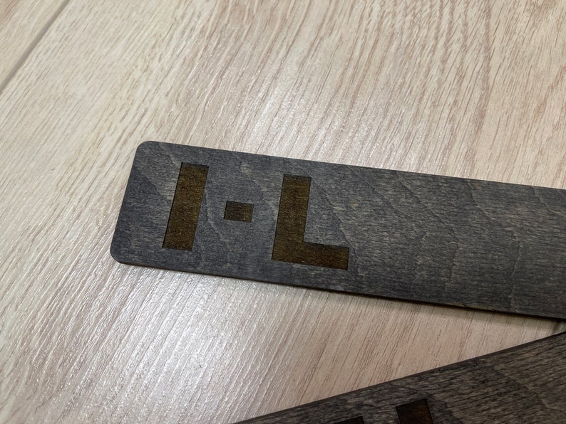 Puede incluir: Un letrero de madera gris oscuro con las letras "I-L" grabadas en un color marr&oacute;n m&aacute;s claro.