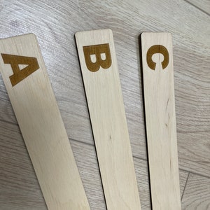Puede incluir: Tres palos de madera con las letras A, B y C grabadas en ellos. Los palos est&aacute;n dispuestos en forma de abanico sobre una superficie de madera marr&oacute;n claro.