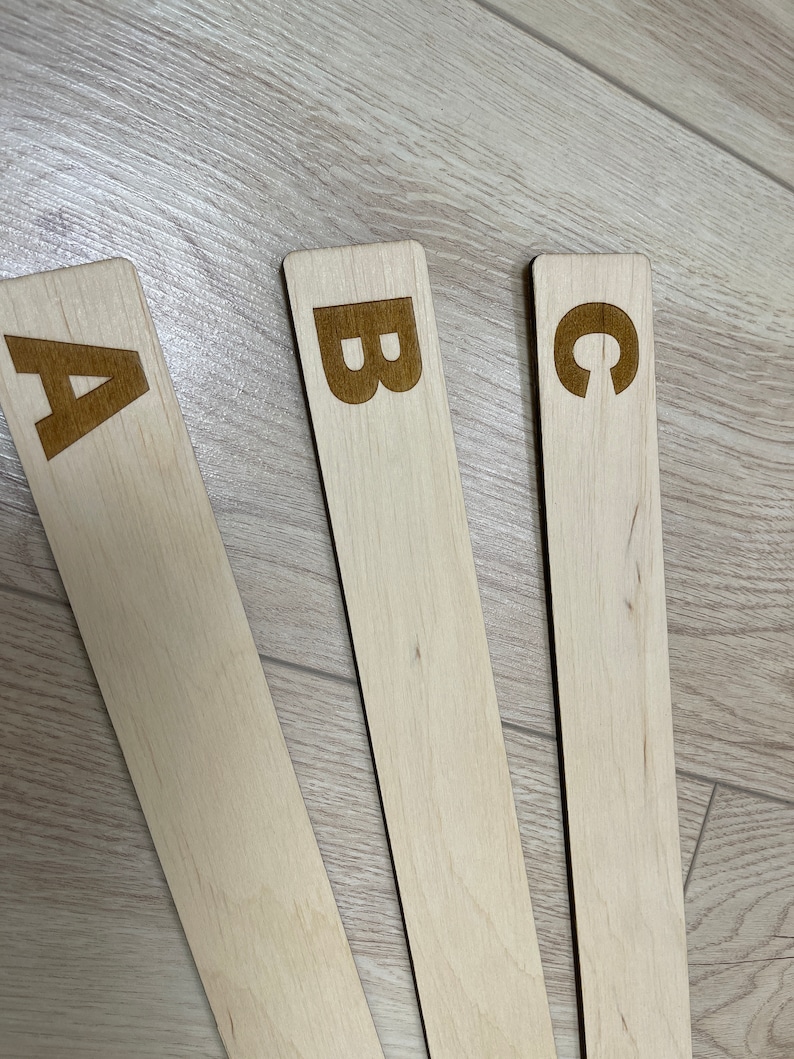 Puede incluir: Tres palos de madera con las letras A, B y C grabadas en ellos. Los palos est&aacute;n dispuestos en forma de abanico sobre una superficie de madera marr&oacute;n claro.