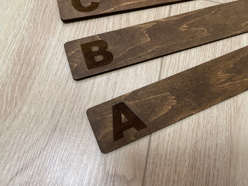 Puede incluir: Tres marcap&aacute;ginas de madera con las letras A, B y C grabadas en ellos. Los marcap&aacute;ginas son de color marr&oacute;n y tienen una veta de madera natural.