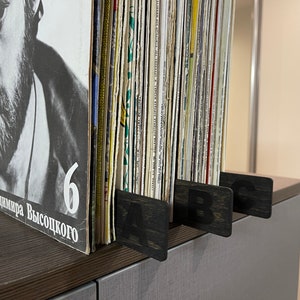 Puede incluir: Primer plano de una estanter&iacute;a de discos de vinilo organizada por letras. La estanter&iacute;a tiene separadores de madera negra etiquetados con "A", "B" y "C".