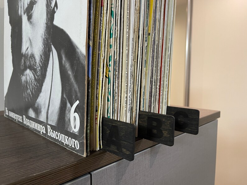 Puede incluir: Primer plano de una estanter&iacute;a de discos de vinilo organizada por letras. La estanter&iacute;a tiene separadores de madera negra etiquetados con "A", "B" y "C".