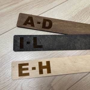 Puede incluir: Tres separadores de alfabeto de madera con las letras A-D, E-H e I-L impresas en ellos. Los separadores son de diferentes tonos de marr&oacute;n.