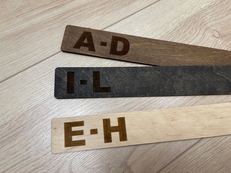 Puede incluir: Tres separadores de alfabeto de madera con las letras A-D, E-H e I-L impresas en ellos. Los separadores son de diferentes tonos de marr&oacute;n.