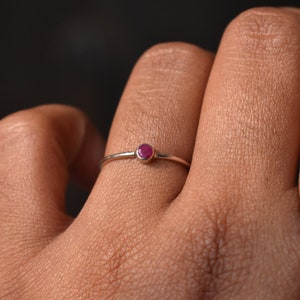 May include: A silver ring with a small, round, red gemstone.