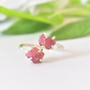 May include: A silver ring with two pink raw gemstone accents. The ring is adjustable and can be worn on any finger.