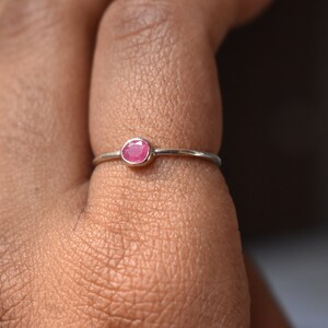 Puede incluir: Un delicado anillo de plata con una pequeña piedra preciosa rosa de forma ovalada engastada en el centro.