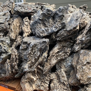 May include: A pile of textured, gray and brown rocks. The rocks have rough surfaces and varying sizes, creating a natural, rugged appearance. Ideal for landscaping or decorative purposes.
