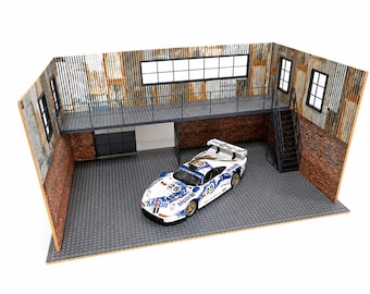 Puede incluir: Un coche de carreras Porsche blanco en miniatura con la marca azul Mobil 1 y el número 25, expuesto en un diorama de garaje detallado con paredes de ladrillo, revestimiento de metal corrugado, un altillo de metal y una escalera.