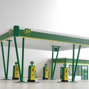 Könnte beinhalten: Ein Modell einer grün-weißen BP-Tankstelle mit vier Zapfsäulen und einem kleinen Gebäude mit einer Autowäsche und einem Shop. Das Gebäude hat ein Schild mit der Aufschrift "BP Shop" und ein grün-weißes BP-Logo.
