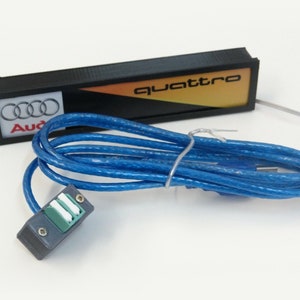 Puede incluir: Un letrero negro y amarillo con la palabra "quattro" en &eacute;l. El letrero est&aacute; conectado a un cable USB azul con un conector negro.