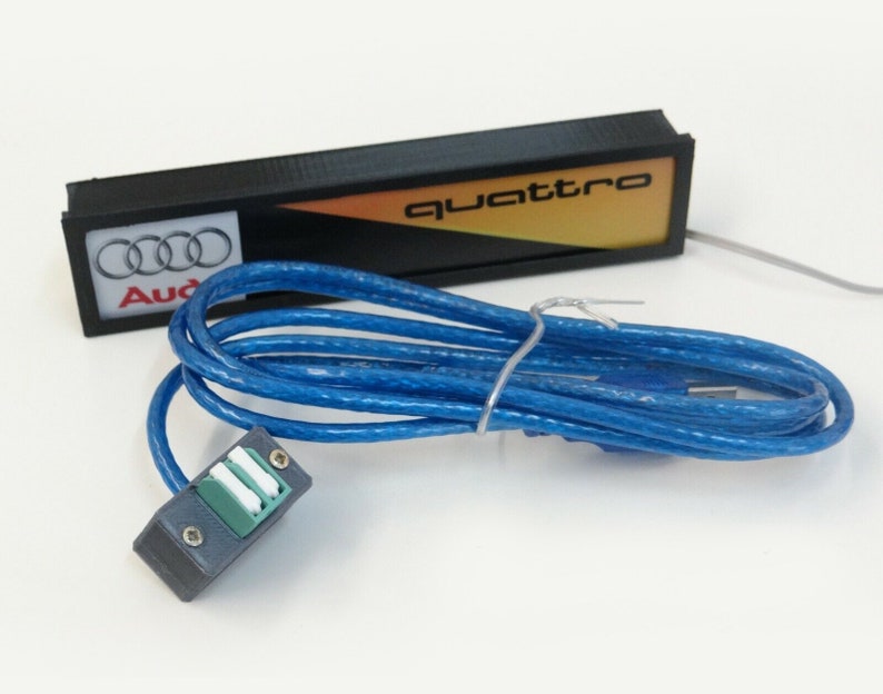 Puede incluir: Un letrero negro y amarillo con la palabra "quattro" en &eacute;l. El letrero est&aacute; conectado a un cable USB azul con un conector negro.