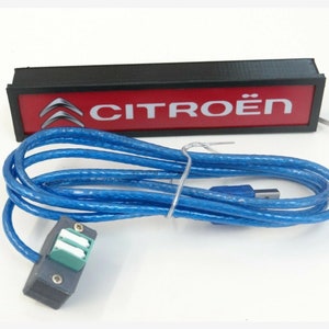 Puede incluir: Una caja rectangular negra con fondo rojo y el texto "CITRO&Euml;N" en blanco. Un cable USB azul est&aacute; conectado a la caja.