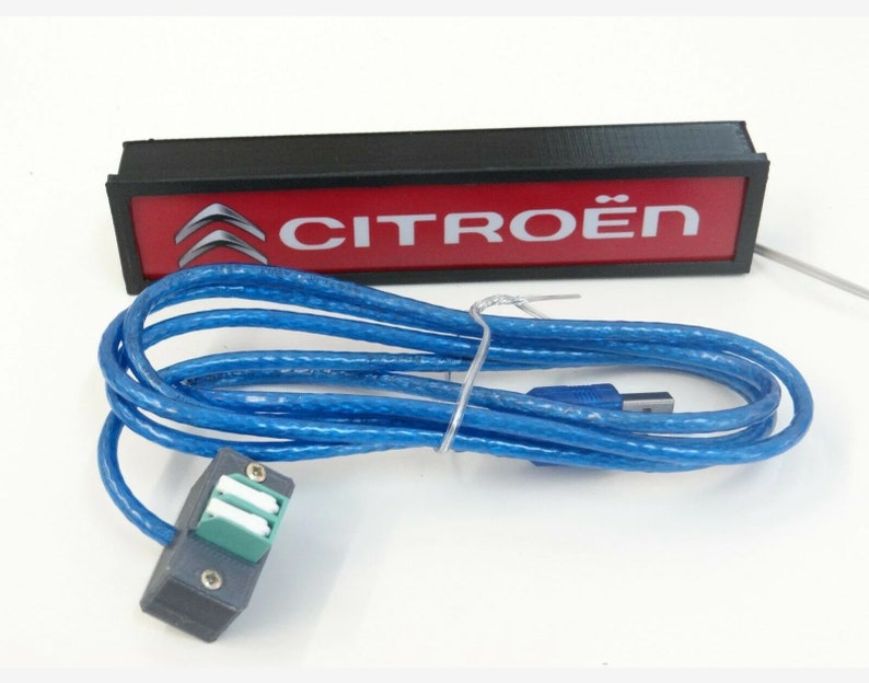 Puede incluir: Una caja rectangular negra con fondo rojo y el texto "CITRO&Euml;N" en blanco. Un cable USB azul est&aacute; conectado a la caja.