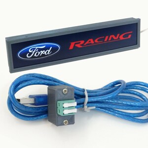 Puede incluir: Un letrero rectangular gris con un logotipo Ford azul y la palabra "RACING" en letras rojas. El letrero est&aacute; conectado a un cable USB azul con un conector gris.