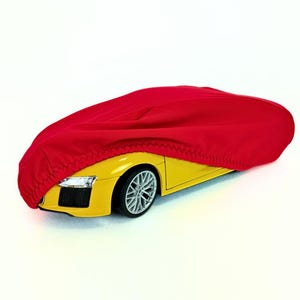 以下が含まれることがあります： 黄色いスポーツカーに部分的に覆われた鮮やかな赤い車のカバー。カバーは滑らかな生地でできており、車両のボディに引っ張られています。車はシルバーのリムと洗練されたデザインで、高性能モデルを示唆しています。