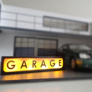 May include: A black and yellow illuminated sign with the word "GARAGE" in white letters.