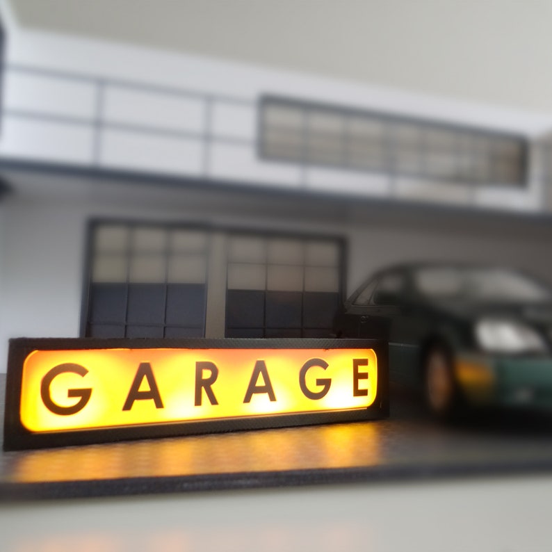 Puede incluir: Un letrero iluminado negro y amarillo con la palabra "GARAGE" en letras blancas.