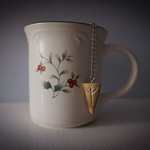 Könnte beinhalten: Eine weiße Keramiktasse mit Blumenmuster und einem hölzernen Tee-Infuser mit einem Runensymbol, das am Henkel hängt.