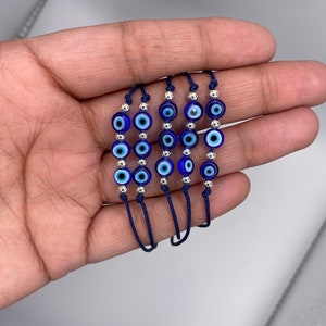 May include: Five blue and white evil eye bracelets with silver beads on navy blue string.