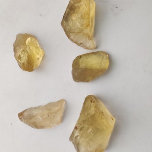 May include: Five rough-cut, translucent yellow gemstones. The stones are various sizes and shapes, with some having a more pointed shape and others being more rounded.