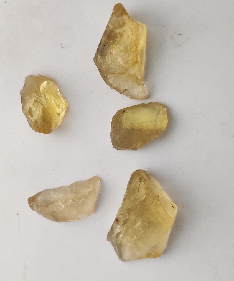 May include: Five rough-cut, translucent yellow gemstones. The stones are various sizes and shapes, with some having a more pointed shape and others being more rounded.