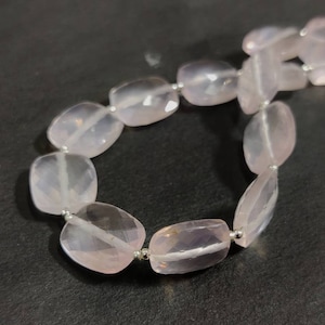 May include: A strand of pale pink rose quartz beads, each bead is faceted and oval shaped. The beads are strung on silver wire.