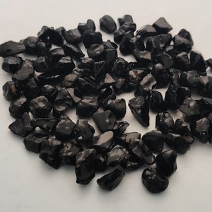 May include: A collection of black obsidian chips, a type of volcanic glass, with a smooth, polished finish. The chips are various sizes and shapes, and have a dark, opaque appearance.