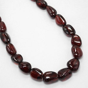 Könnte beinhalten: Eine Kette aus dunkelroten Edelsteinperlen, jede Perle ist glatt und oval geformt.