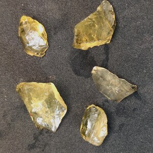 May include: Five pieces of raw, yellow citrine crystals. The crystals are various sizes and shapes, with some having a more pointed shape and others being more rounded.
