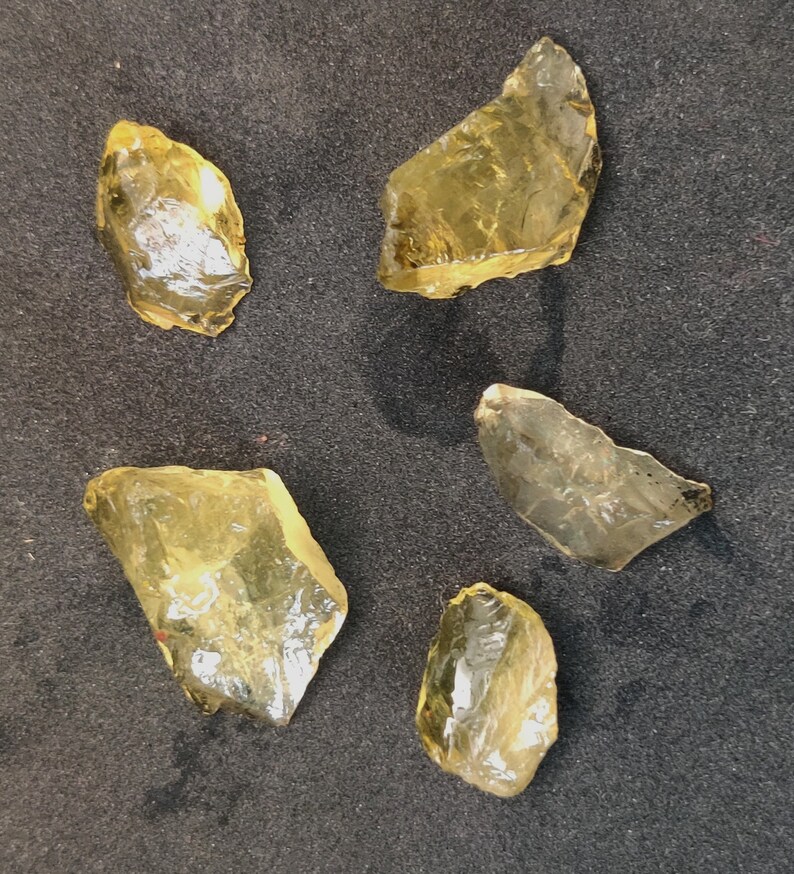 May include: Five pieces of raw, yellow citrine crystals. The crystals are various sizes and shapes, with some having a more pointed shape and others being more rounded.