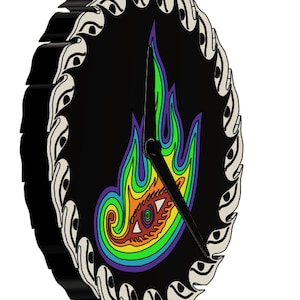 Op de afbeelding: Een ronde zwarte wandklok met een kleurrijk vlamontwerp en een centraal oog. De klok heeft een decoratieve rand met witte en zwarte details en zwarte wijzers. Het vlamontwerp bevat groen, geel, oranje, rood, blauw en paars.