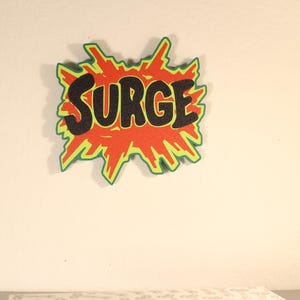 May include: A comic book style graphic with the word "SURGE" in black, outlined in orange, and set against a red and green burst shape. The design is mounted on a white wall.