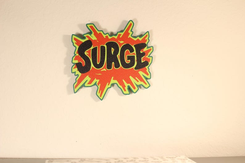 May include: A comic book style graphic with the word "SURGE" in black, outlined in orange, and set against a red and green burst shape. The design is mounted on a white wall.