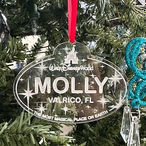 May include: Clear acrylic Walt Disney World Christmas ornament with the name "MOLLY" and location "VALRICO, FL" etched in white. The ornament has a red ribbon for hanging and features the phrase "THE MOST MAGICAL PLACE ON EARTH."