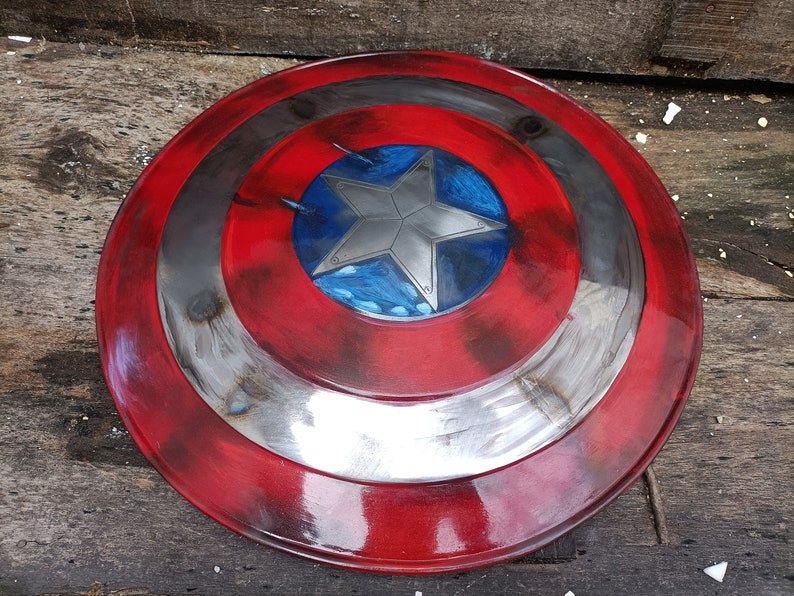 May include: A red, white and blue Captain America shield with a silver star in the centre. The shield has a distressed, weathered look, as if it has been in many battles.