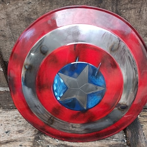 May include: A red, white and blue Captain America shield with a distressed paint finish. The shield has a five-pointed star in the centre.