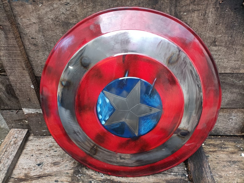 May include: A red, white and blue Captain America shield with a distressed paint finish. The shield has a five-pointed star in the centre.