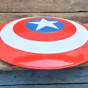 May include: A red, white, and blue Captain America shield with a white star on a blue circle in the center. The shield is made of plastic and has a glossy finish.