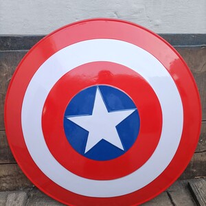 May include: A red, white, and blue Captain America shield with a five-pointed white star on a blue background. The shield is round and has a raised edge.
