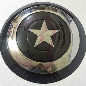 Puede incluir: Una r&eacute;plica de escudo de Capit&aacute;n Am&eacute;rica negro y plateado. El escudo tiene una gran estrella de cinco puntas en el centro.
