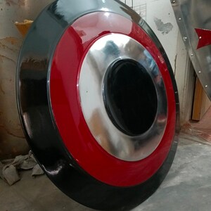May include: A round shield with a black outer ring, a red middle ring, and a silver inner ring. The center is black. The shield is a prop or decorative item.