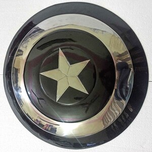 Puede incluir: Una r&eacute;plica de escudo de Capit&aacute;n Am&eacute;rica negro y plateado. El escudo tiene una gran estrella blanca de cinco puntas en el centro.