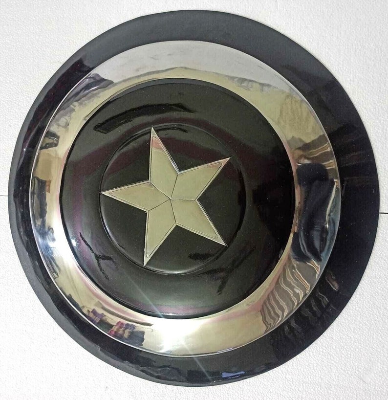Puede incluir: Una r&eacute;plica de escudo de Capit&aacute;n Am&eacute;rica negro y plateado. El escudo tiene una gran estrella blanca de cinco puntas en el centro.
