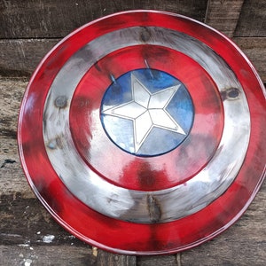 May include: A red, white and blue Captain America shield with a five-pointed star in the centre. The shield is made of metal and has a distressed look.