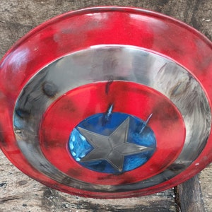 May include: A red, white and blue Captain America shield with a distressed paint finish. The shield has a five-pointed star in the centre.