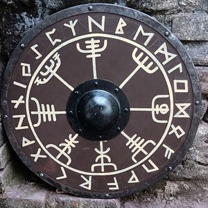 May include: A round, brown wooden shield with a black metal rim and a central boss. The shield is decorated with white runes and the letters "FYNBMXI" around the edge.