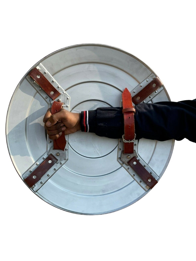 May include: A silver round shield with a red leather strap and metal rivets. The shield has a raised centre and is held by a hand.